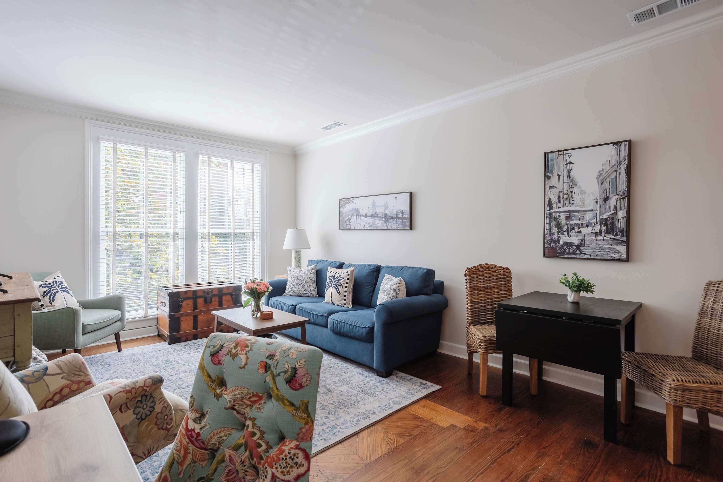 Una sala de estar con un sofá azul, un sillón estampado, una mesa de centro de madera y una silla de mimbre.