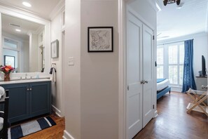 A hallway leading to a bedroom with a large window, a bathroom with a vanity, and a framed picture on the wall. - Amazing Location| King Bed| Cute Downtown Condo (Savannah)