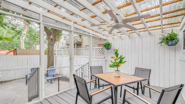Un patio techado con una mesa, sillas, ventilador de techo y plantas en macetas.