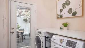 Un área de lavandería con lavadora y secadora, una pequeña mesa con sillas y una planta en maceta sobre una encimera.