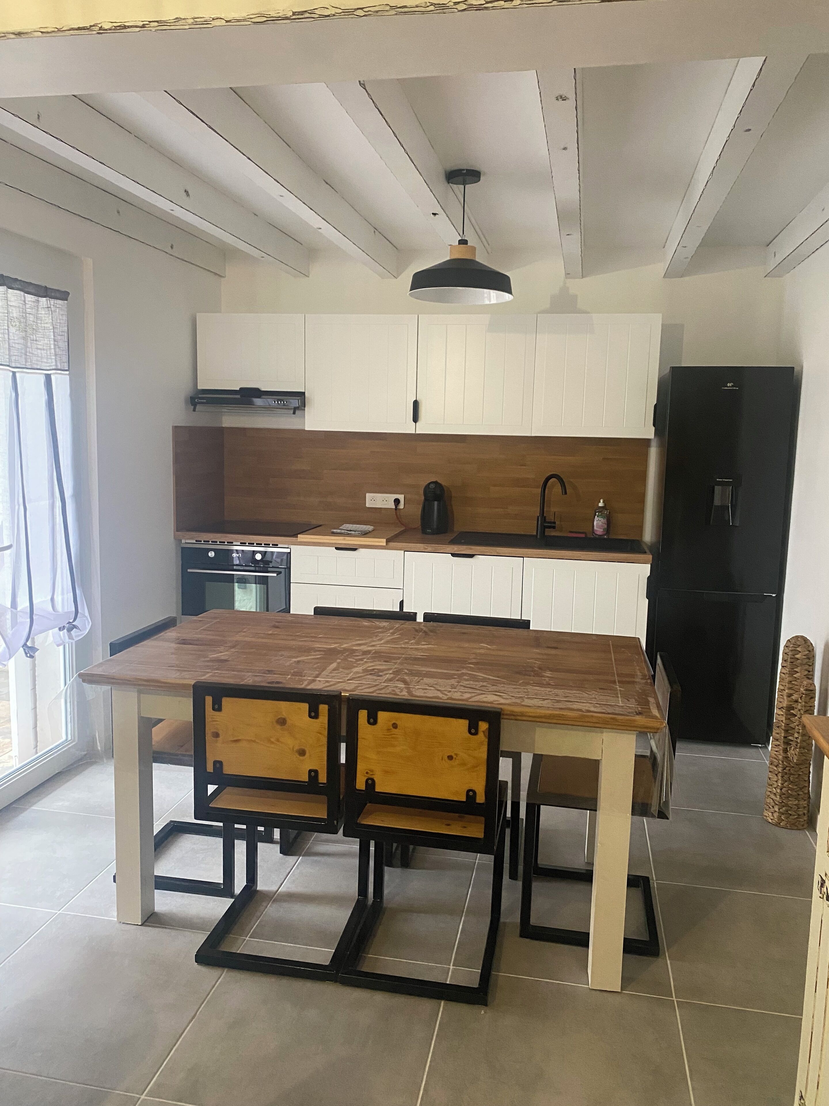 A modern kitchen with white cabinets, a black refrigerator, and a wooden dining table with chairs.