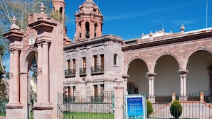 A historic building with a central tower, arched walkways, and a fenced courtyard. - Hotel Guadalupe Express (Guadalupe)
