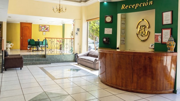 A reception area with a green wall, a wooden reception desk, and a chandelier. - Hotel Guadalupe Express (Guadalupe)