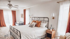 Une chambre bien rangée, avec un lit, des tables de chevet, une chaise et un ventilateur de plafond.