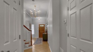 Un couloir avec des portes blanches, un escalier en bois, un lustre et un tapis sur le sol.