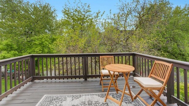 Une terrasse en bois avec une table et deux chaises, entourée d’une végétation luxuriante et d’arbres.