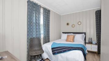 A bedroom with a bed, a chair, a nightstand, and a window with patterned curtains.