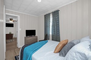 A bedroom with a bed, a dresser, a television, and a ceiling fan.