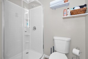 A bathroom with a glass-enclosed shower, a toilet, and a shelf with toiletries.