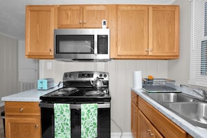 A kitchen with wooden cabinets, a stainless steel microwave, a stove, a toaster, and a sink. - Cozy Room & Private Bath Near VA Medical Center (Fayetteville)