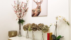 A white table with various vases of flowers and a framed painting of a deer.