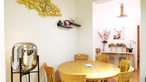 A dining area with a round wooden table, six wooden chairs, a round mirror, and a decorative gold wall piece.
