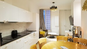 A modern kitchen with white cabinets, a black countertop, and a built-in oven. There is a dining area with a wooden table and chairs, a small round table, and a unique light fixture.
