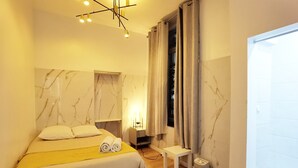 A bedroom with a bed, bedside table, lamp, and a window with curtains.