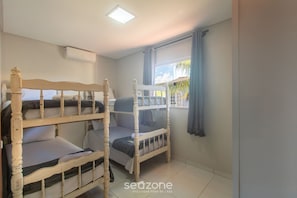 Um quarto com beliches, janela com cortinas, ar condicionado e piso ladrilhado.