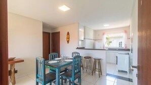 Un comedor con una mesa y sillas de madera, una cocina con refrigerador y una ventana con cortinas.