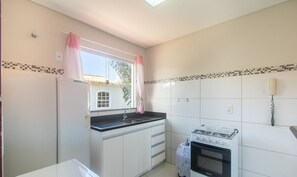 A compact kitchen with white cabinets, a gas stove, a sink, and a window with pink curtains. - Apt in Condo w/ Pool 850m From the Beach - Srr0007 (Porto Seguro)