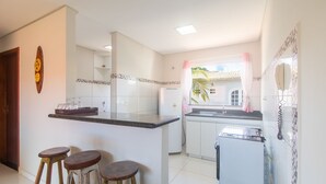 A modern kitchen with a central island, a refrigerator, and a window with a view of a house. There are three stools and a decorative wall clock.