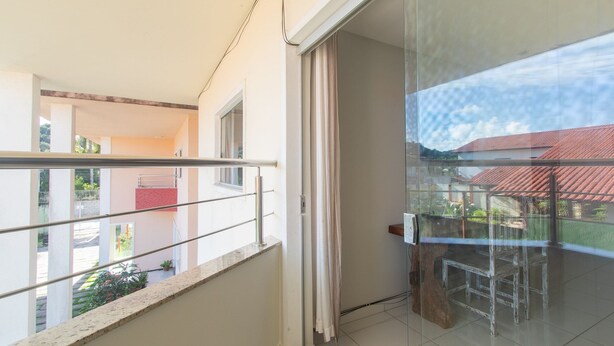 Un balcón con puerta de cristal, barandilla metálica y vista a un edificio de techos rojos.