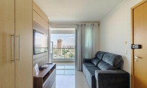 A modern living room with a sofa, a flat-screen TV, and a view of a cityscape through large windows.
