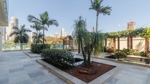 A rooftop garden with palm trees, a wooden gazebo, and a small pond. - Estúdio em Cond no Setor Bueno CEL1804 (Goiânia)
