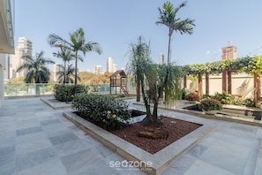 A rooftop garden with palm trees, a wooden gazebo, and a small pond. - Estúdio em Cond no Setor Bueno CEL1804 (Goiânia)