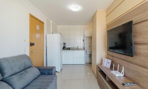 A modern living room with a grey sofa, a TV mounted on a wooden wall, and a kitchen in the background.