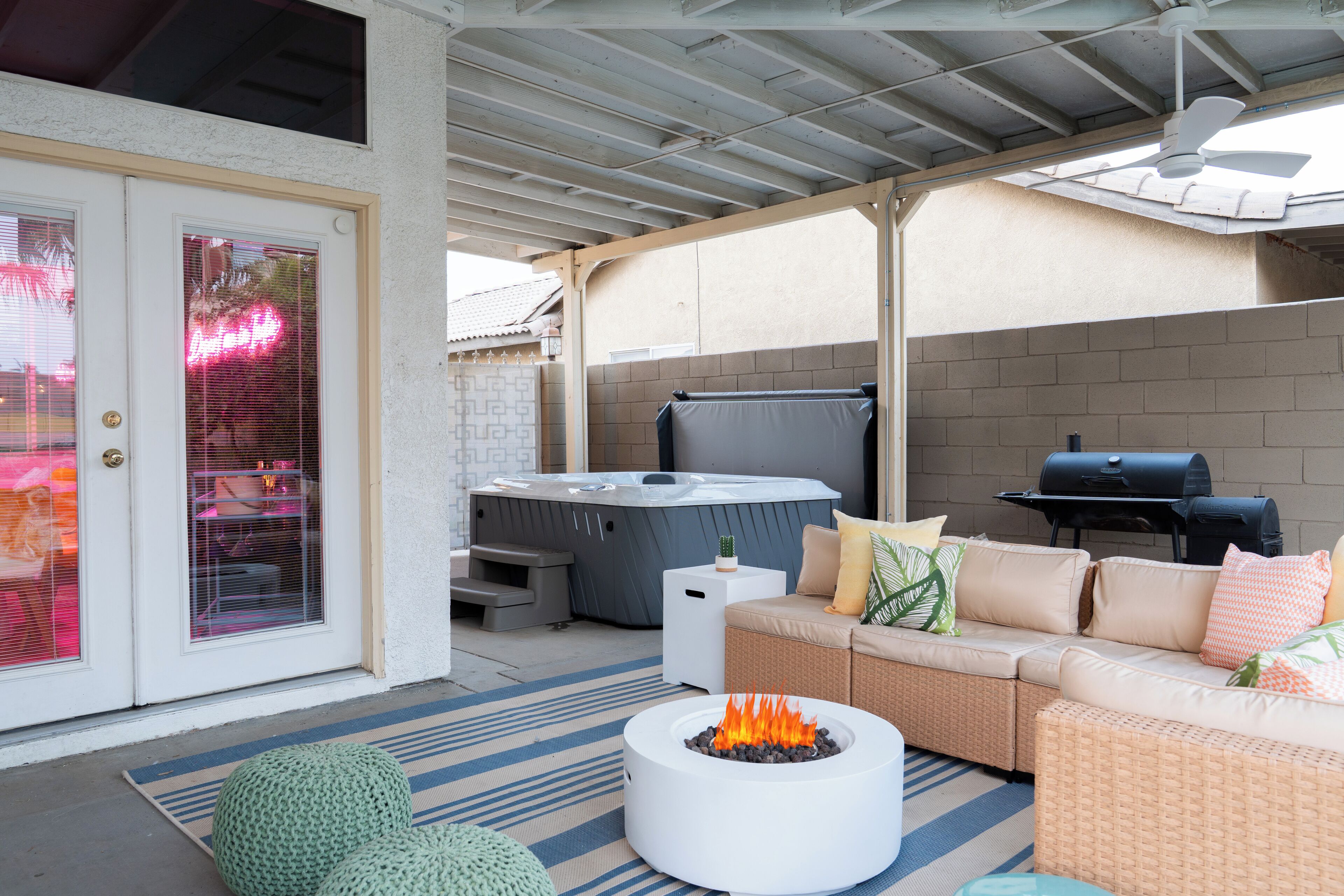 A covered patio area with a fire pit, outdoor seating, a hot tub, and a grill.