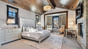A bedroom with a large bed, a dresser, a chair, a table, and a fireplace. - Ski-in Ski-out Deer Valley Hot Tub, Fire Pit, Views Silver Sun by Avantstay (Park City)