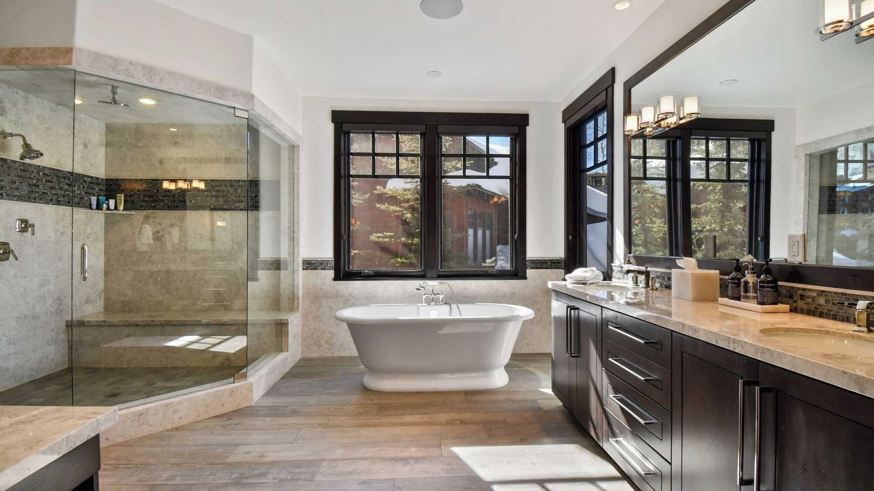 A modern bathroom with a freestanding bathtub, a glass-enclosed shower, and a large window providing a view of the outside.