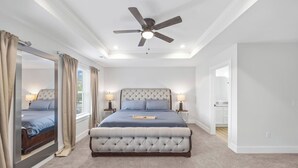 Una camera da letto con un letto grande, una ventola a soffitto e vista sulla cucina.