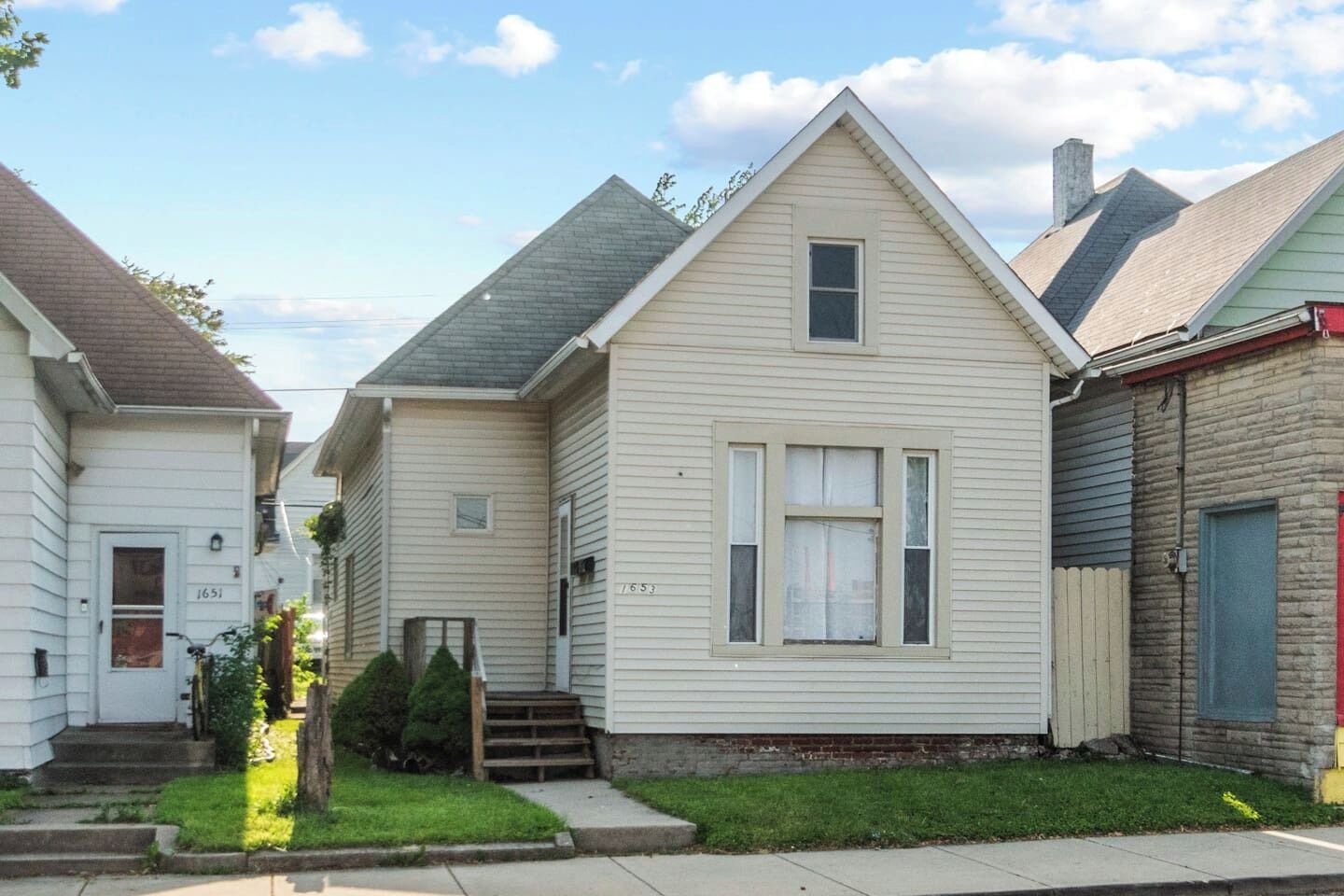 A row of single-story houses with front porches, a small front yard, and a clear sky.