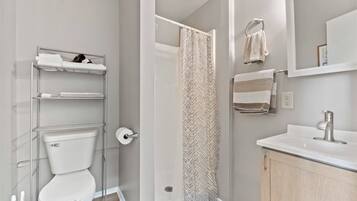 A bathroom with a toilet, a shower with a patterned curtain, a sink with a modern faucet, and a towel rack with multiple towels.