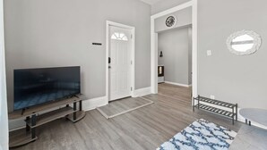 A modern living room with a flat-screen TV on a wooden stand, a bench, and a patterned rug.