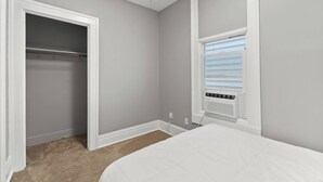 A bedroom with a closet, a window with blinds, and a carpeted floor.