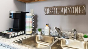 A kitchen with a coffee maker, a mug rack, a bottle of eucalyptus mint soap, and a sign that says "COFFEE, ANYONE?"