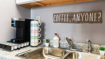 A kitchen with a coffee maker, a mug rack, a bottle of eucalyptus mint soap, and a sign that says "COFFEE, ANYONE?"
