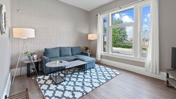 A modern living room with a grey sofa, a round coffee table, a patterned rug, a standing lamp, and a ceiling fan.