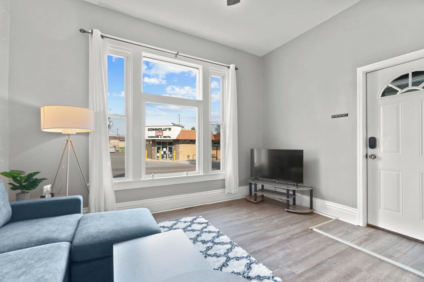 A modern living room with a large window, a flat-screen TV, a sofa, and a lamp.