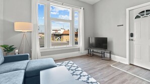 A modern living room with a large window, a flat-screen TV, a sofa, and a lamp.