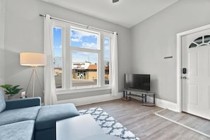 Uma sala de estar moderna com uma janela ampla, uma TV de tela plana, um sofá e uma luminária.