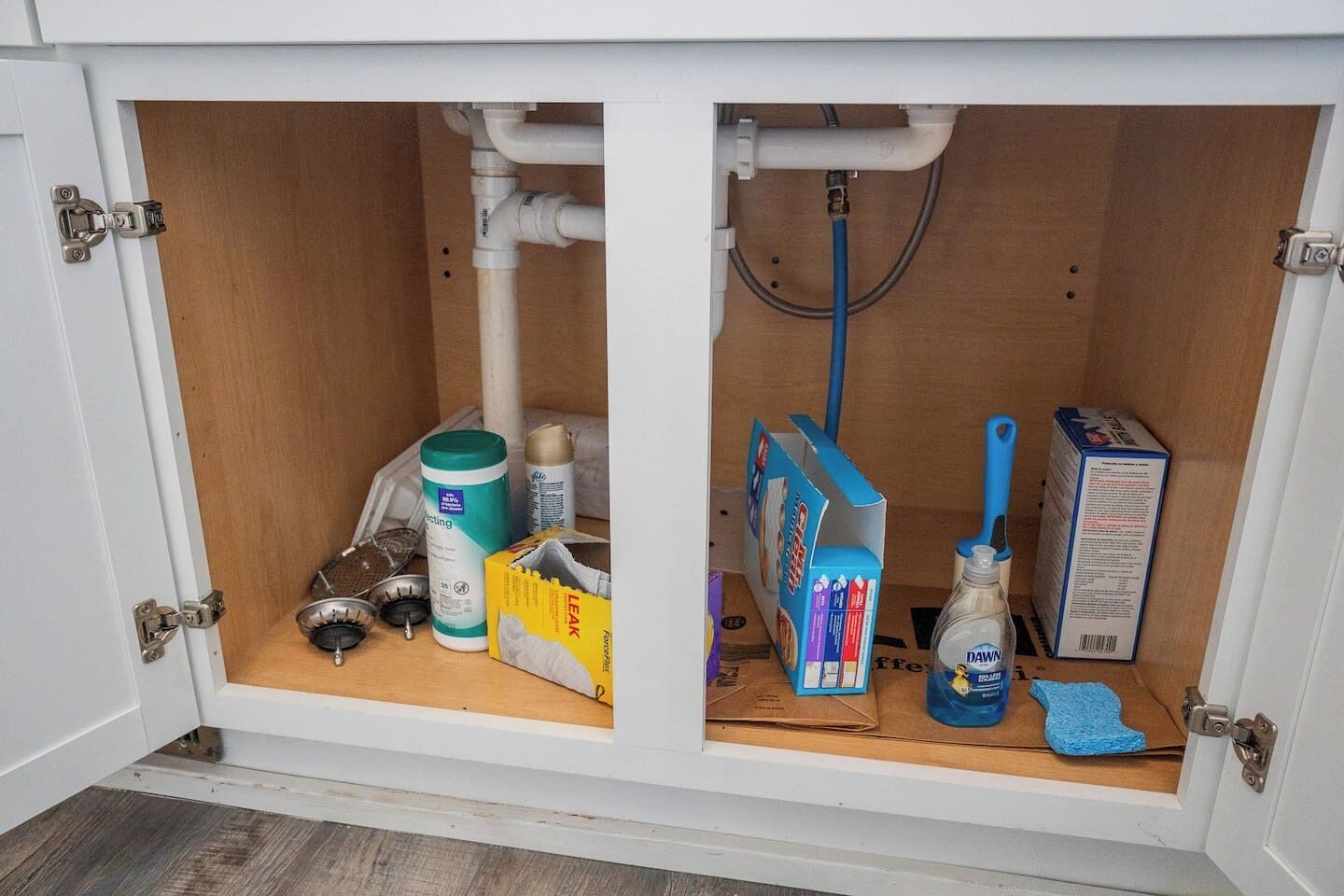 A kitchen cabinet with a wooden door, a white interior, and various cleaning supplies.