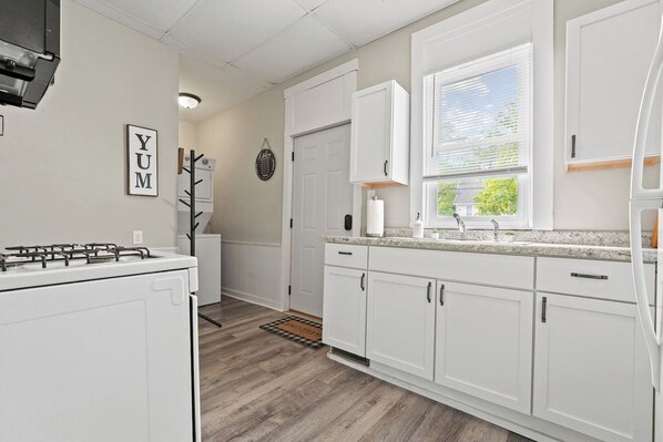 A modern kitchen with white cabinetry, a built-in stove, and a window with blinds.