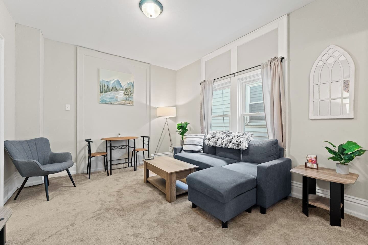 Un salon moderne avec un canapé gris, une petite table en bois, un fauteuil gris et une lampe sur pied.