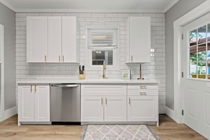 A modern kitchen with white cabinetry, a dishwasher, and a window with blinds.