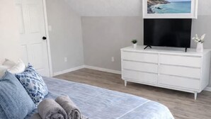 Un dormitorio con cama, cómoda, televisor y un cuadro en la pared.