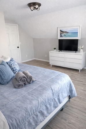 Ein Schlafzimmer mit Bett, Kommode, Fernseher und einem Bild an der Wand.