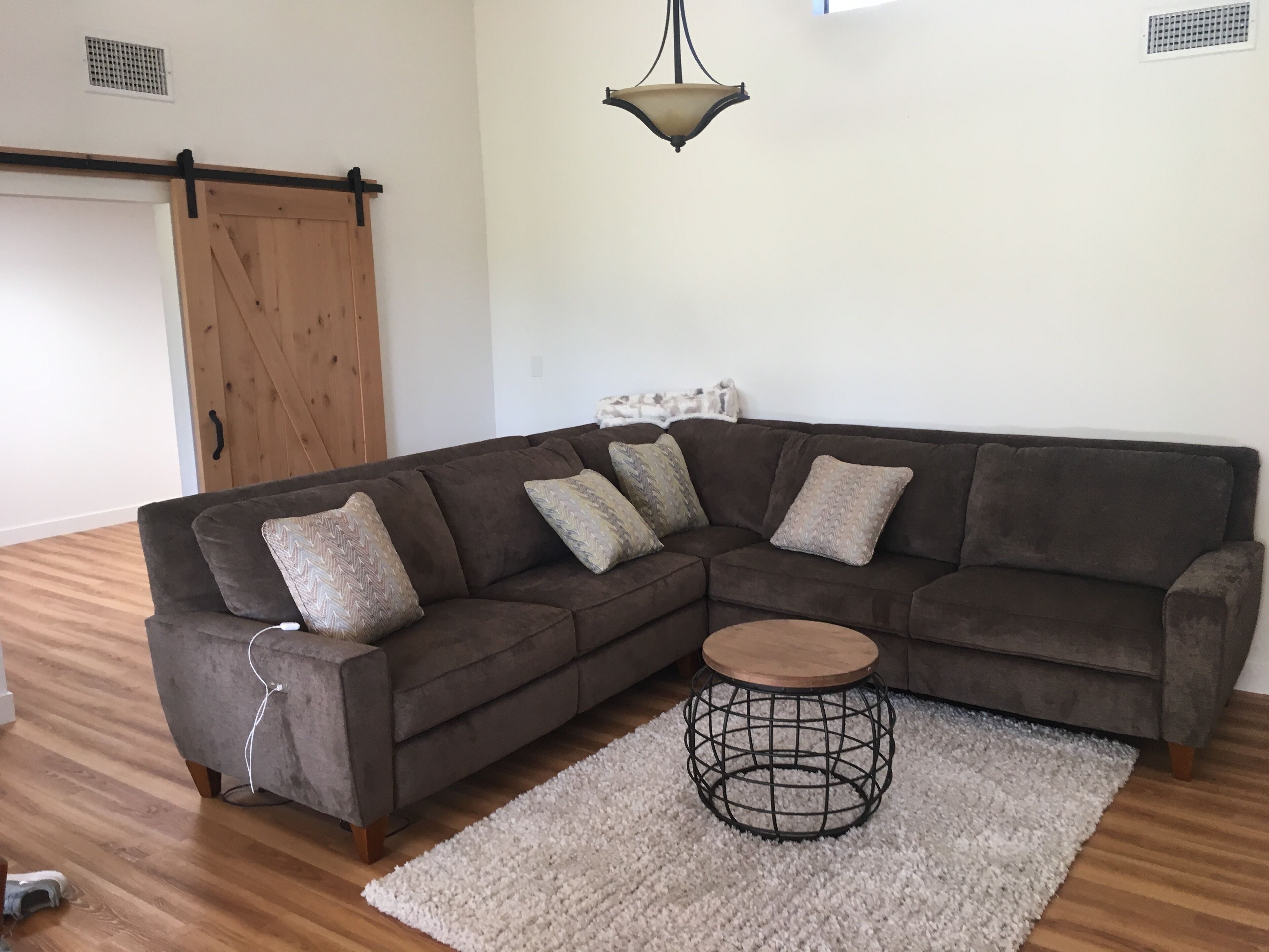 A living room with a sectional sofa, a round coffee table, a white rug, and a hanging light fixture.