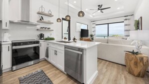 Een moderne keuken met een centraal eiland, een inbouwoven en een zithoek met een bank en een televisie.