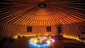 Een joert met een rond lichtarrangement op de vloer, een centrale paal en een lattenwand.